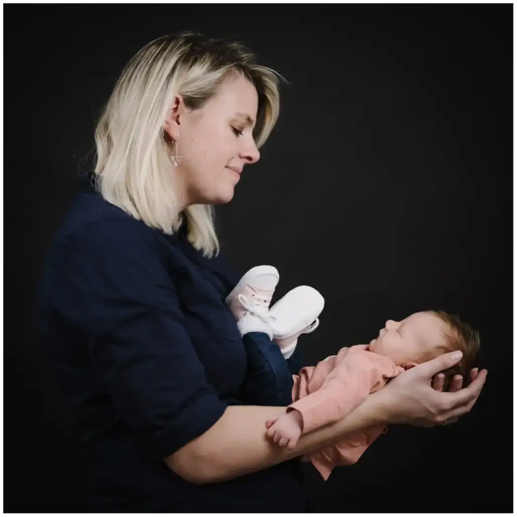 Mère regardant son nouveau-né endormi dans ses bras pendant une séance photo de naissance sur fond noir.