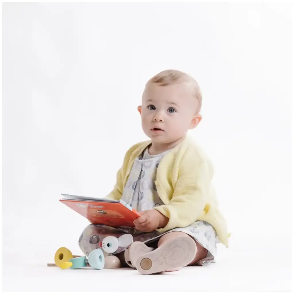 Jeune enfant assis avec un livre rouge et des jouets en bois pendant une séance photo de petite enfance.