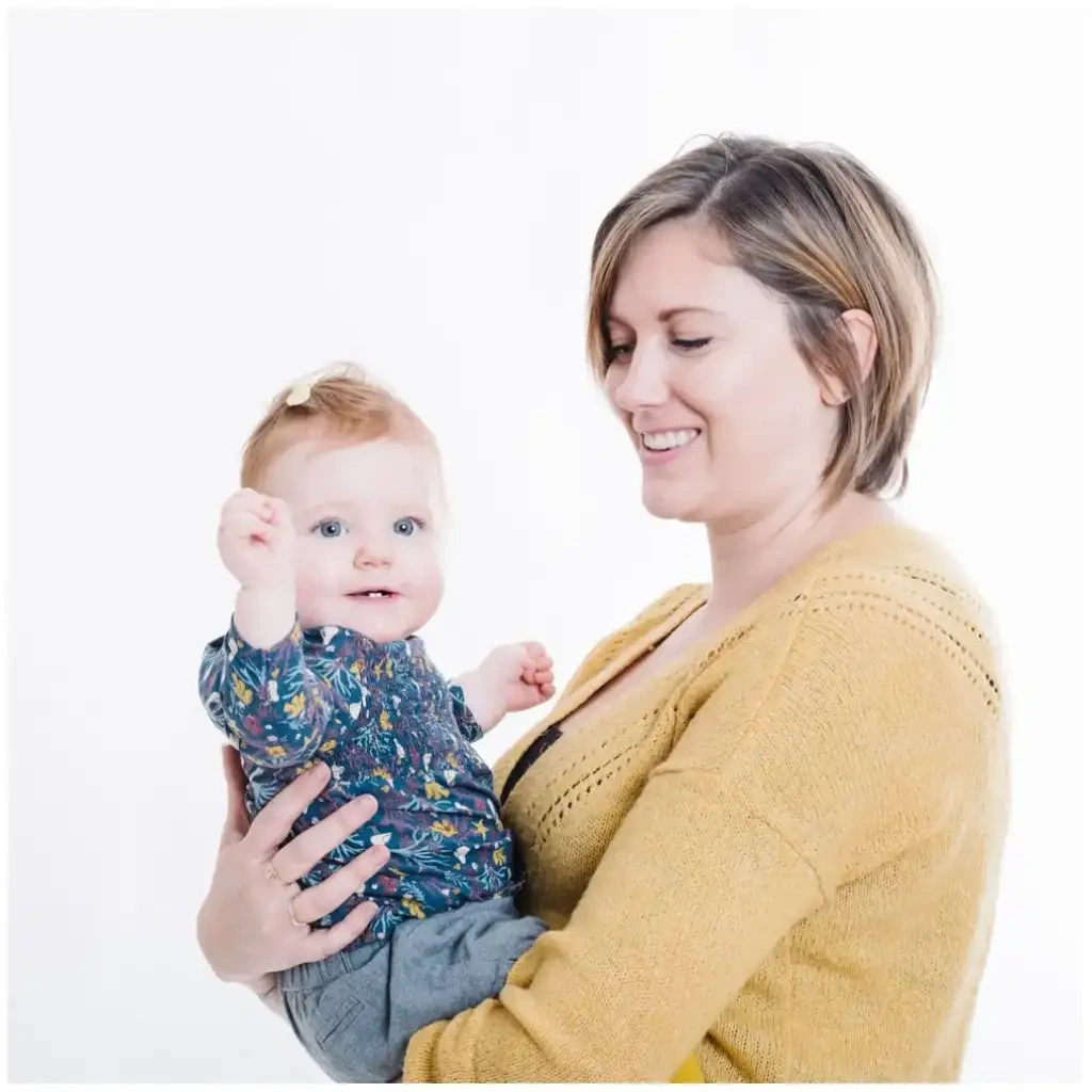 Mère souriante portant son bébé dans ses bras pendant une séance photo de naissance lumineuse.