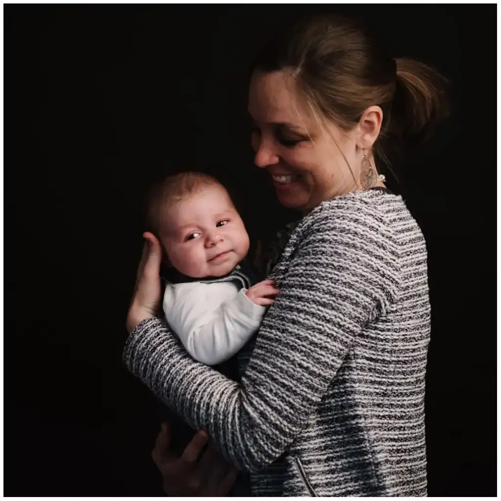 Mère souriante tenant son bébé contre elle pendant une séance photo de naissance.