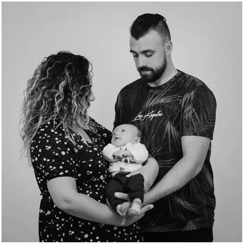 Deux parents tenant leur nouveau-né dans leurs bras pendant une séance photo de naissance en noir et blanc.