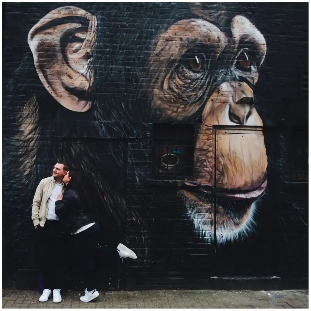 Couple posé au pied d’une grande fresque urbaine représentant un chimpanzé.
