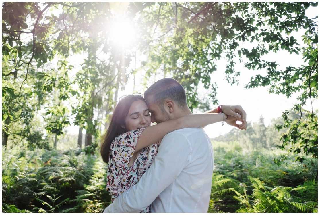 Couple enlacé dans une forêt de fougères lors d'une séance photo d'engagement.