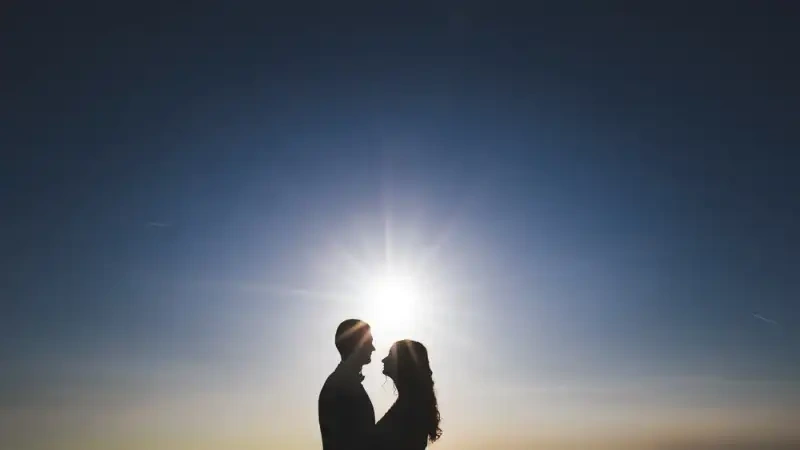 Silhouette d’un couple face à face devant le soleil sous un ciel bleu profond.