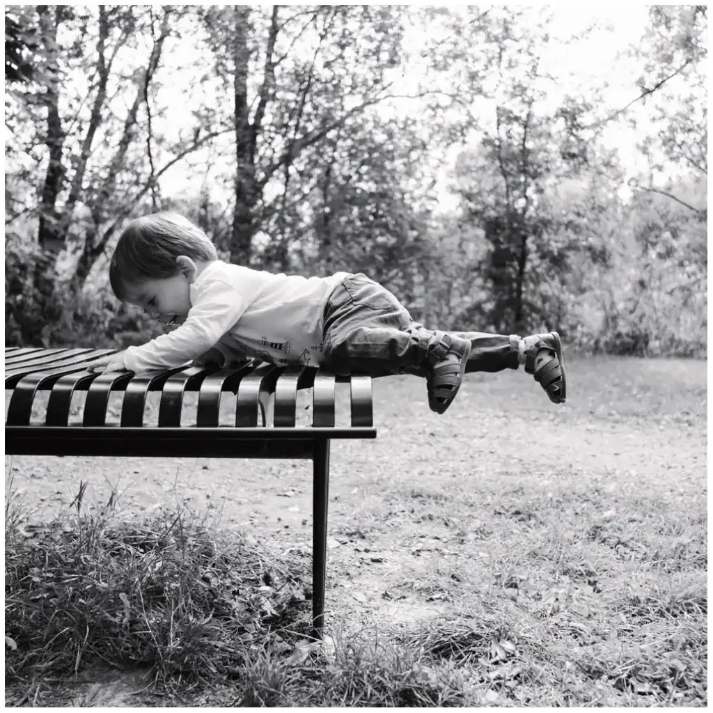 Jeune enfant allongé sur un banc dans un parc boisé lors d’une séance photo de famille.
