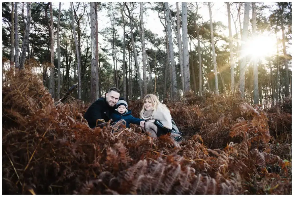 Couple avec son bébé assis dans les fougères d’une forêt pendant une séance photo de famille.
