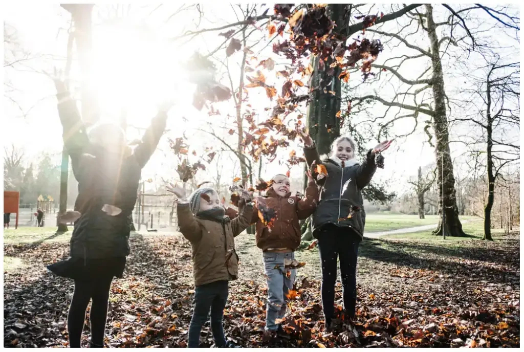 Quatre enfants lançant des feuilles mortes dans un parc boisé lors d’une séance photo de famille.