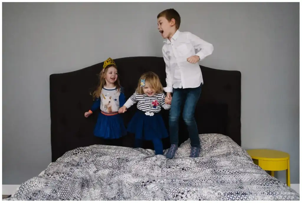 Trois enfants riant et sautant sur un lit pendant une séance photo de famille.