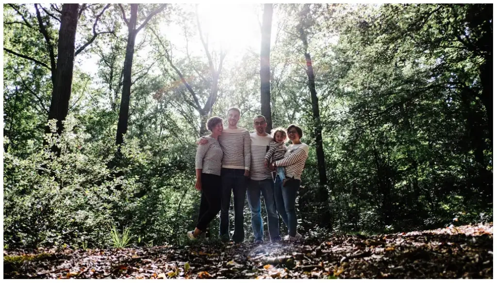 Cinq membres d'une famille réunis dans une forêt sous une lumière en contre-jour.
