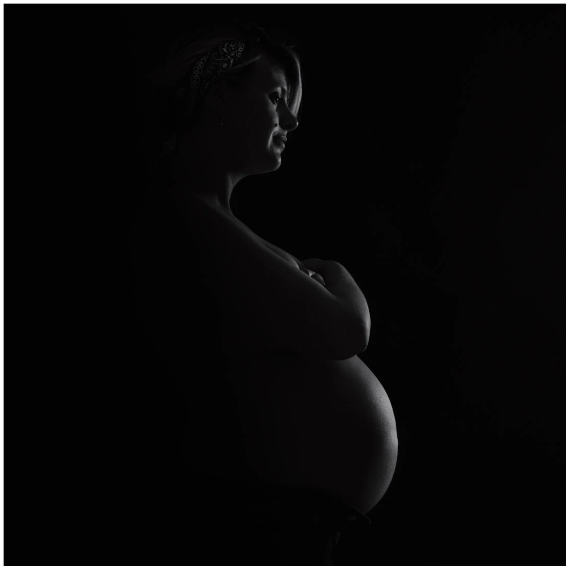 Portrait en clair-obscur d'une femme enceinte de profil sur fond noir.