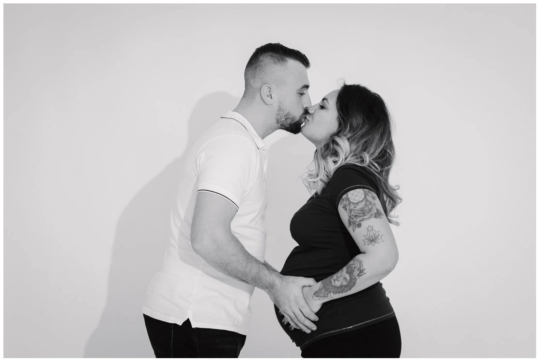 Couple s'embrassant et tenant le ventre de la future mère pendant une séance photo de grossesse en noir et blanc.