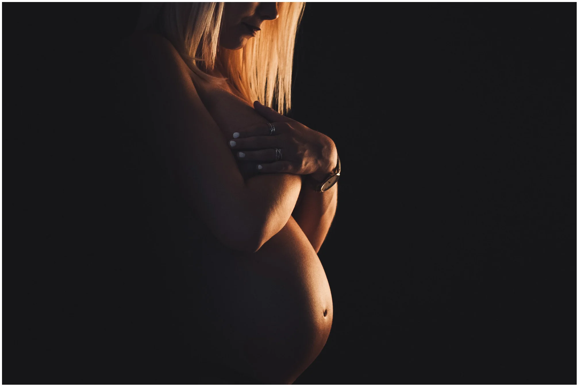 Deux enfants posant leurs mains sur le ventre d'une femme enceinte pendant une séance photo de grossesse en noir et blanc.