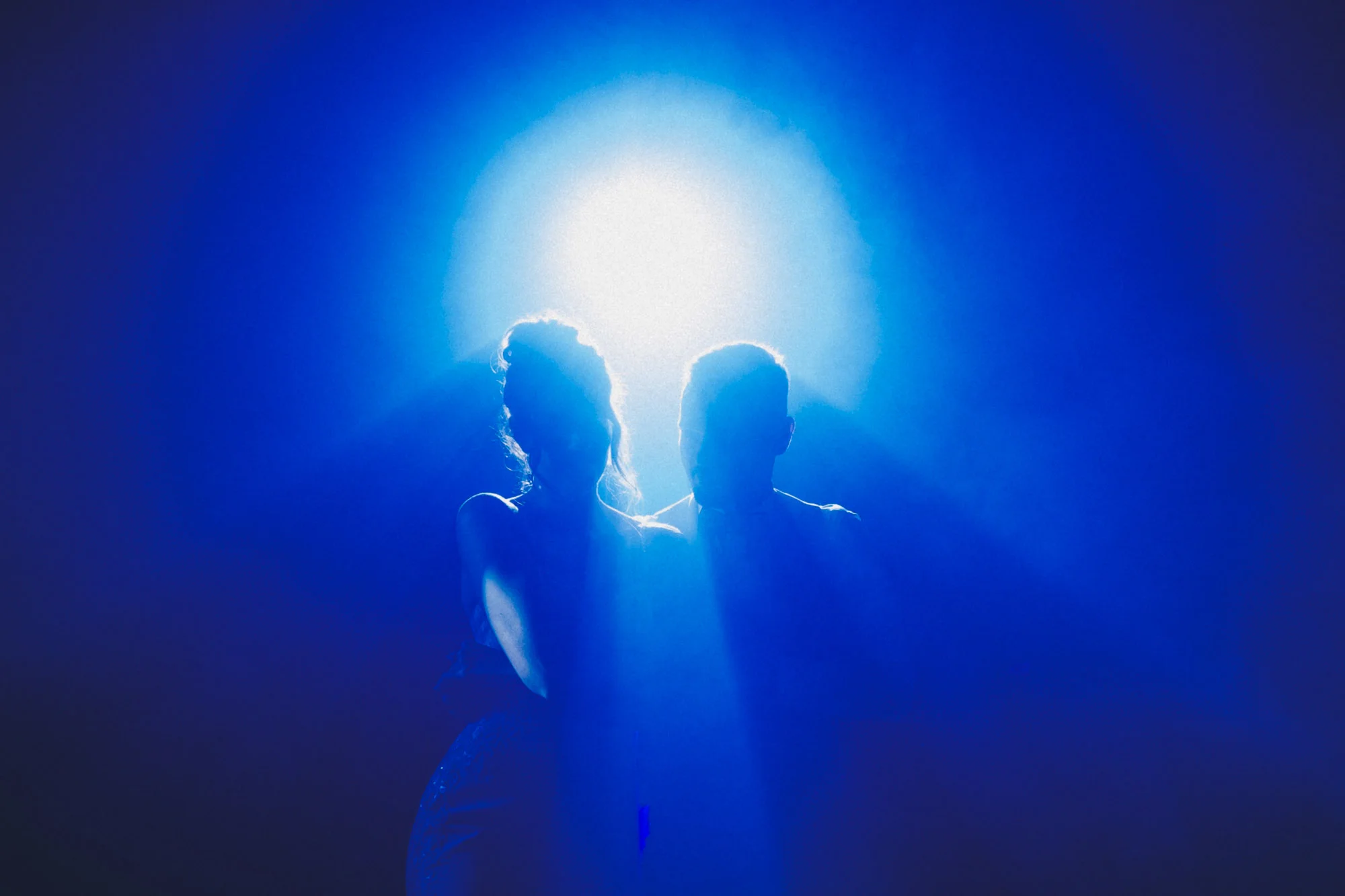 Silhouette d'un couple de mariés devant une lumière bleue intense.