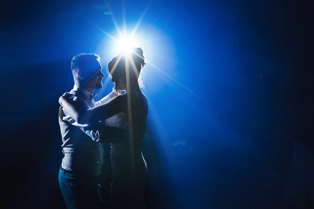 Mariés enlacés pendant leur danse sous un projecteur bleu lors d’un reportage de mariage.