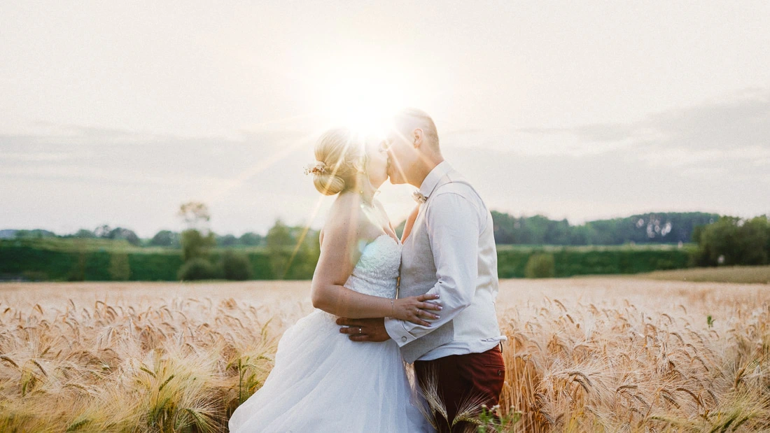 Mariés s'embrassant dans un champ de céréales dorées au soleil couchant lors d'un reportage de mariage.