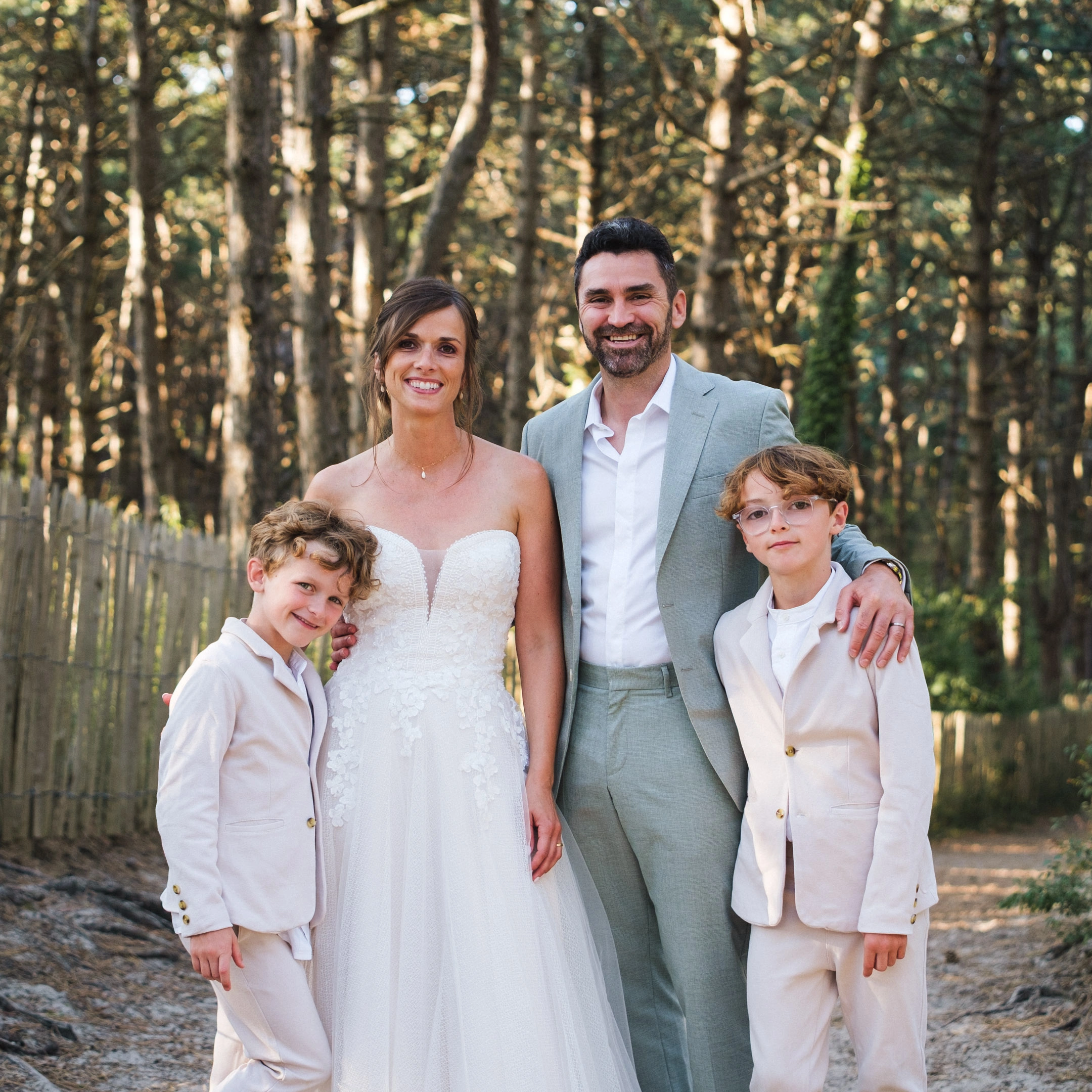Caroline et Anthony en tenue de mariage entourés de leurs deux enfants dans une forêt de pins.