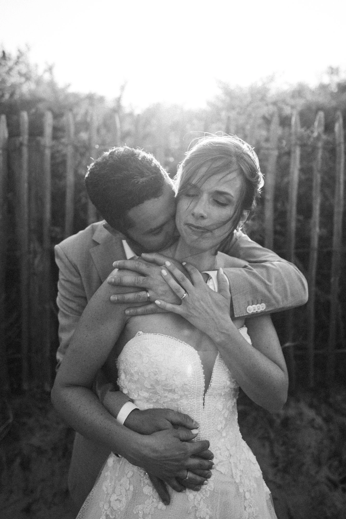 Anthony enlaçant Caroline par-derrière dans un portrait en noir et blanc réalisé en forêt.