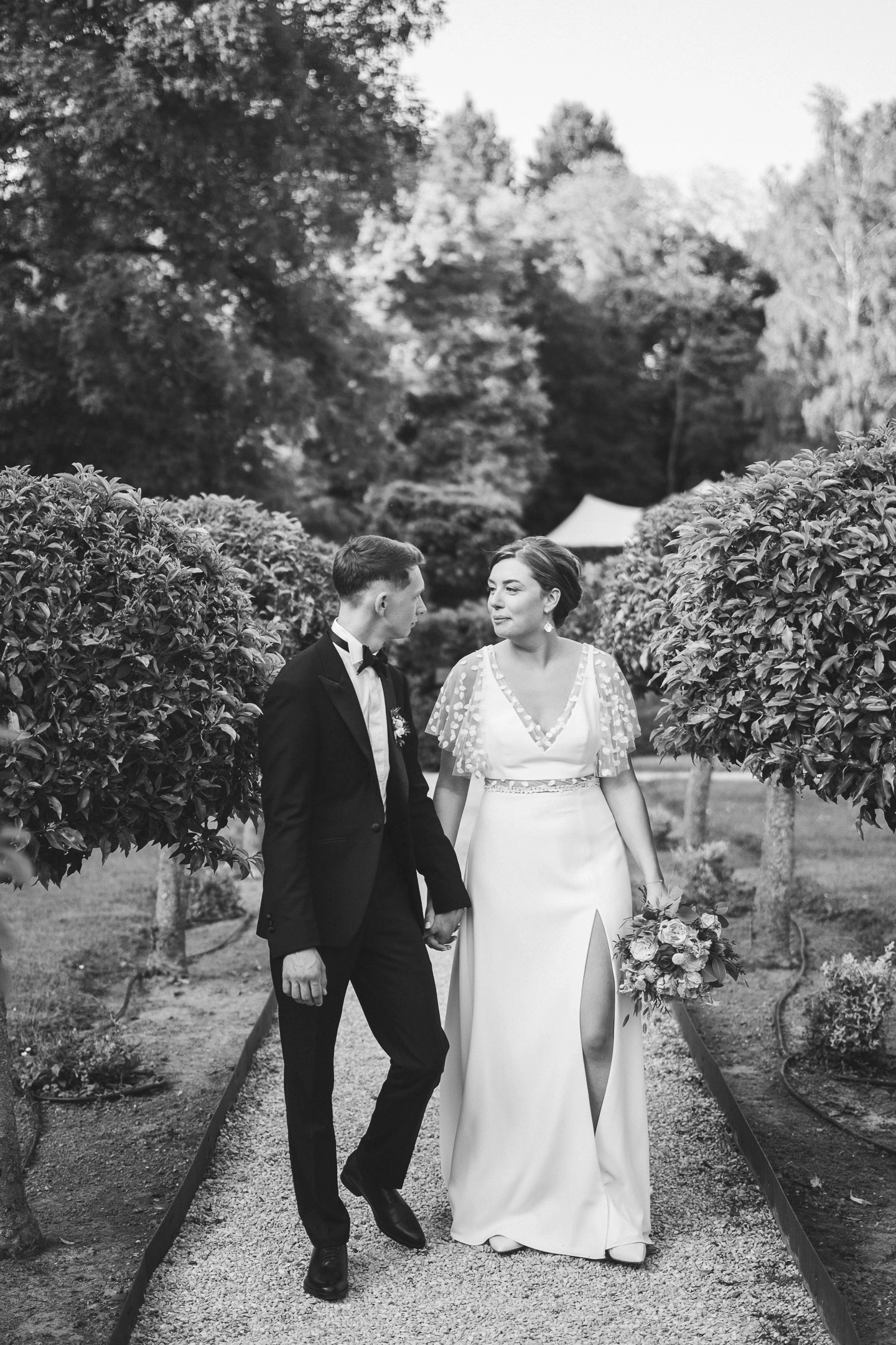 Célia et Louis marchant main dans la main dans un jardin, photographiés en noir et blanc.