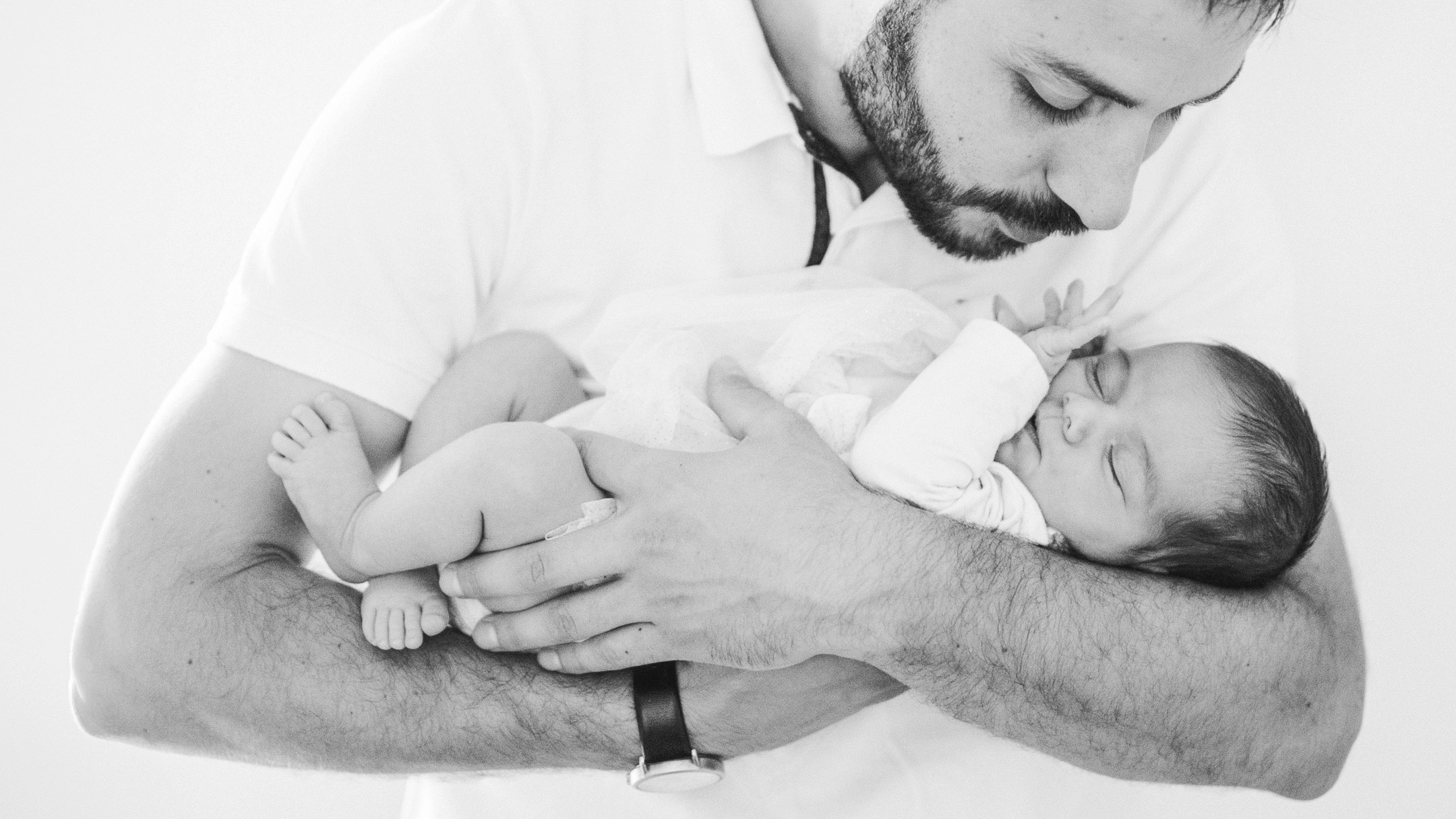 Un père regarde son nouveau-né allongé dans ses bras dans un portrait en noir et blanc.