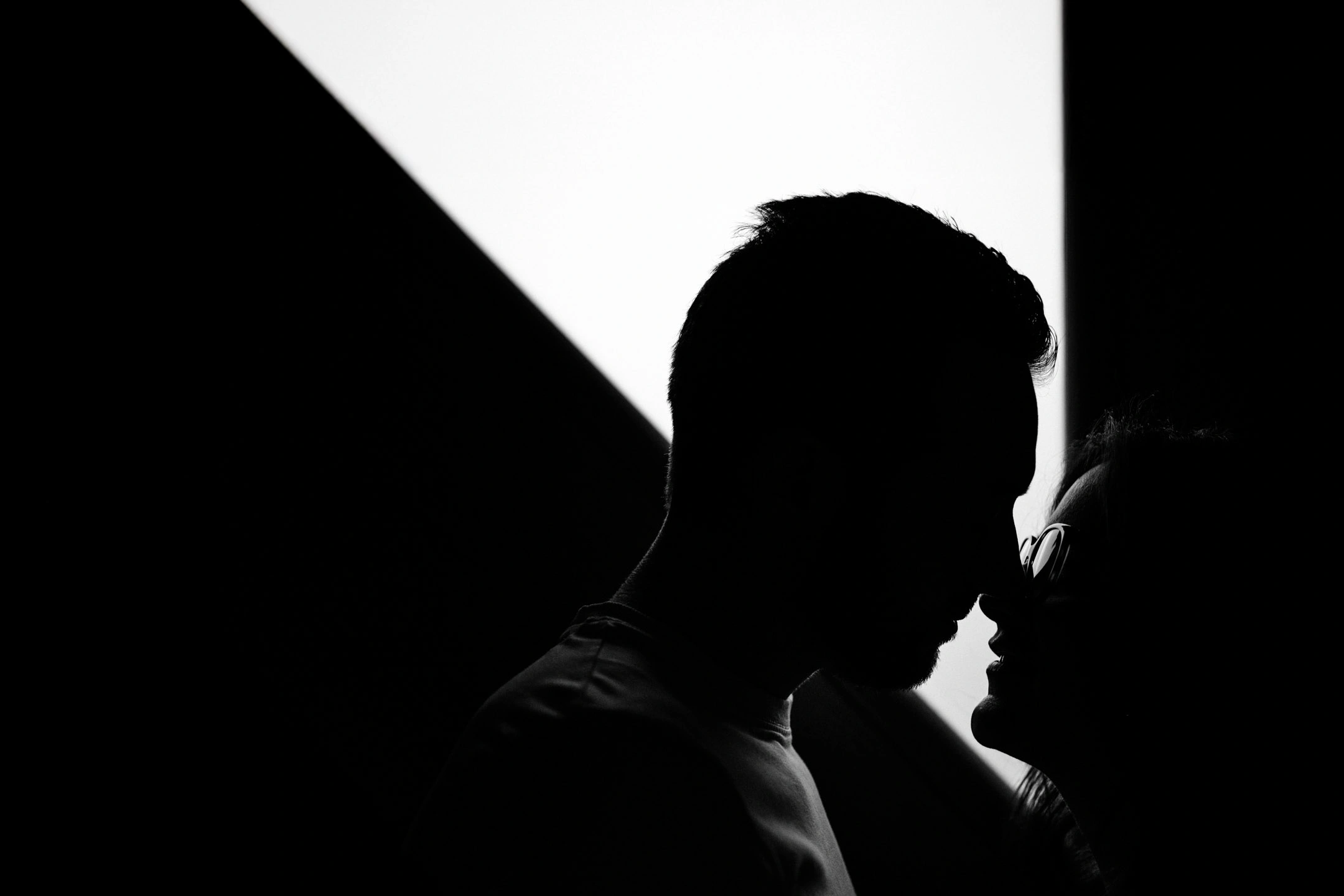 Couple de profil, front contre front, en silhouette devant une lumière géométrique en noir et blanc.