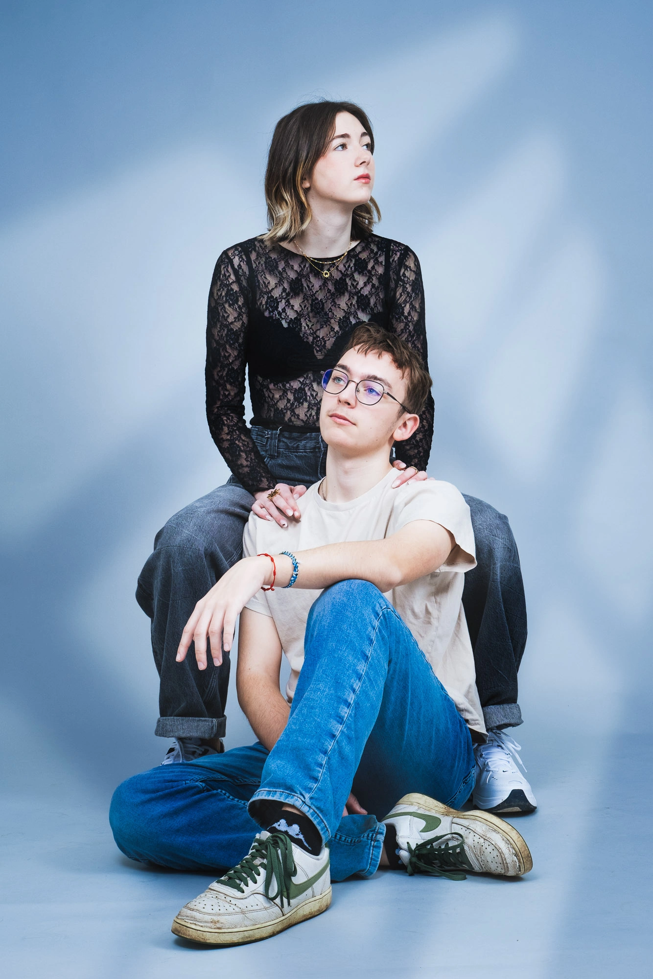 Jeune couple posé devant un fond bleu clair, l’homme assis au premier plan et la femme derrière lui.