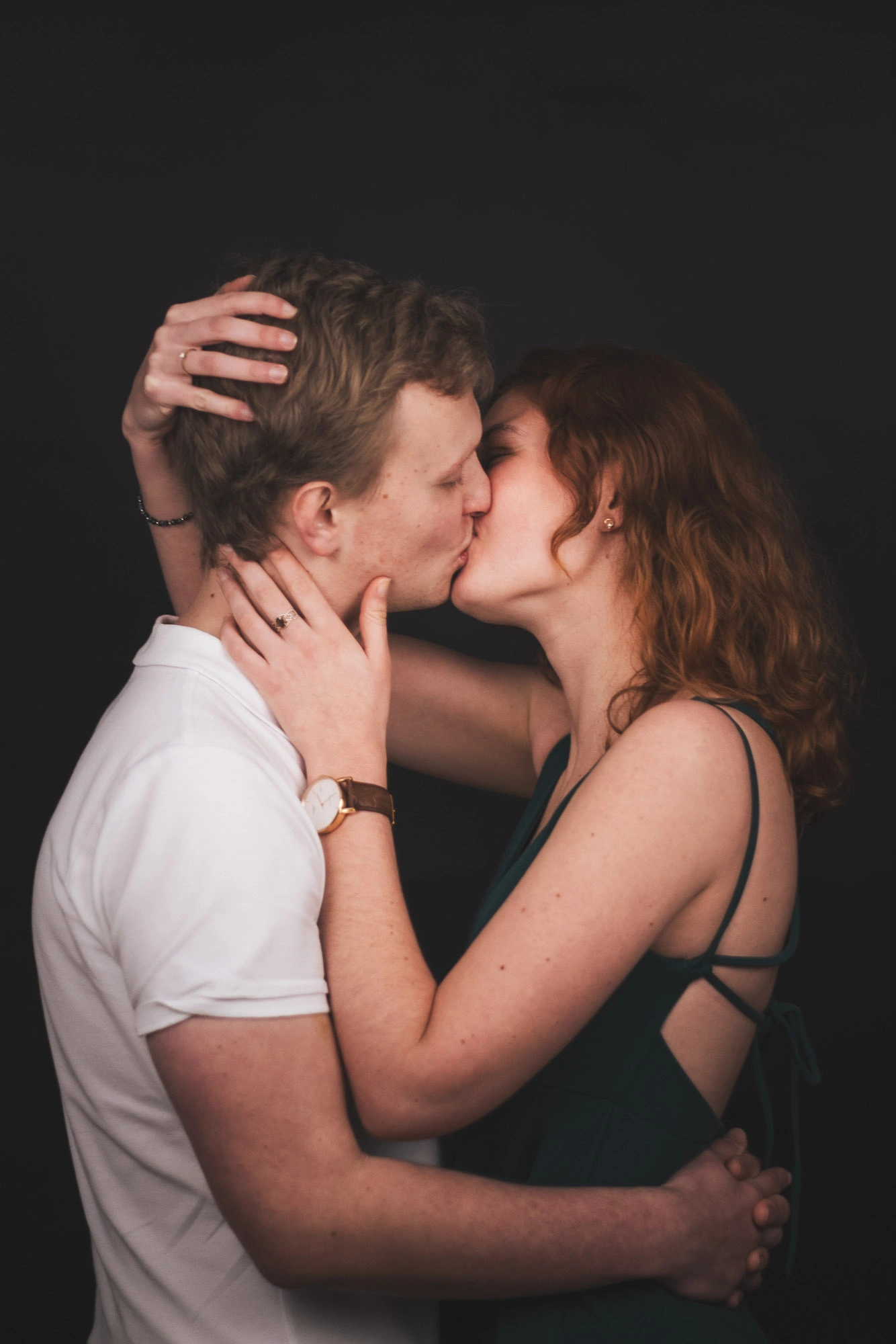 Couple s’embrassant sur fond noir, la femme entourant le visage de son compagnon de ses mains.