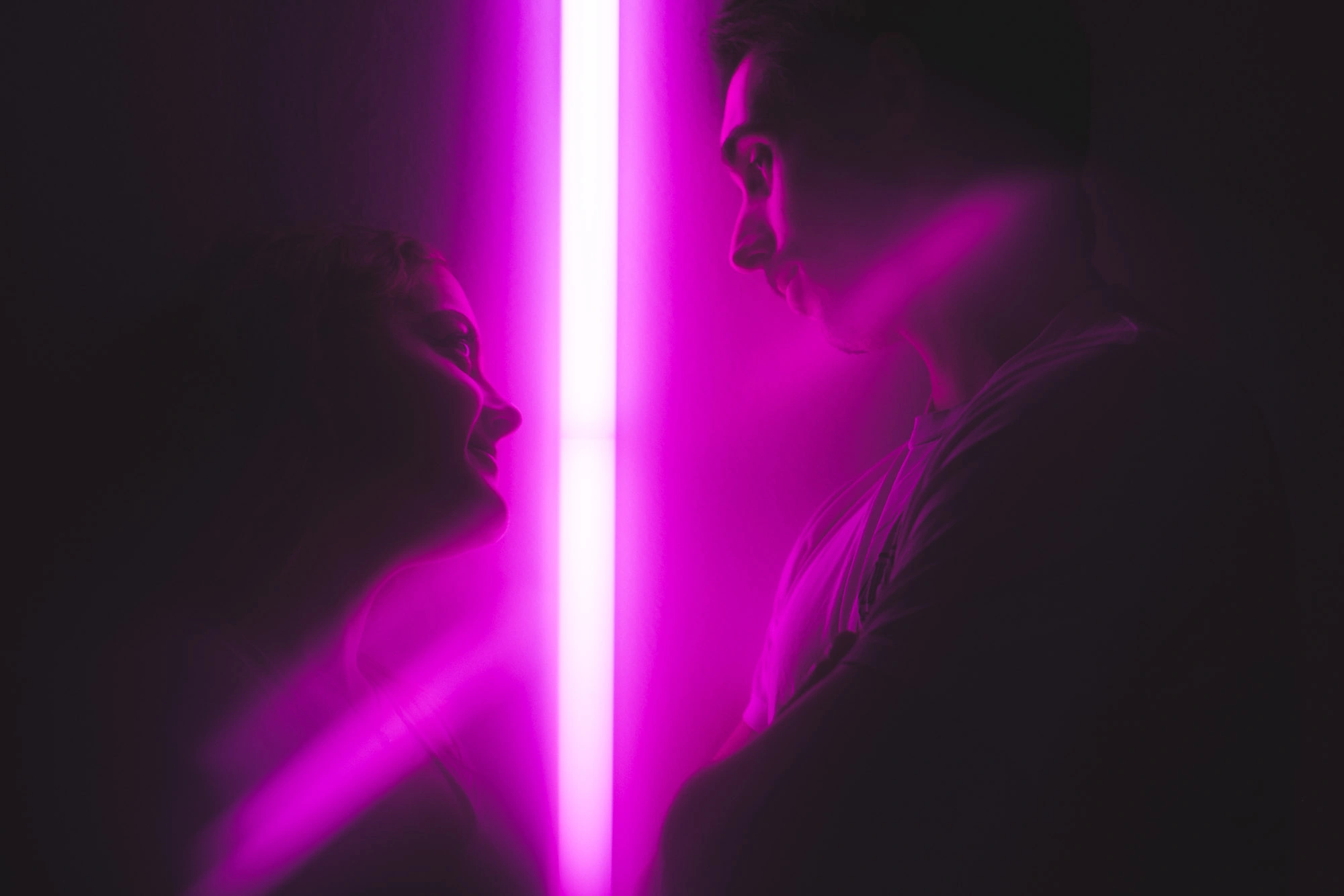 Couple face à face de part et d’autre d’une lumière verticale rose et violette.