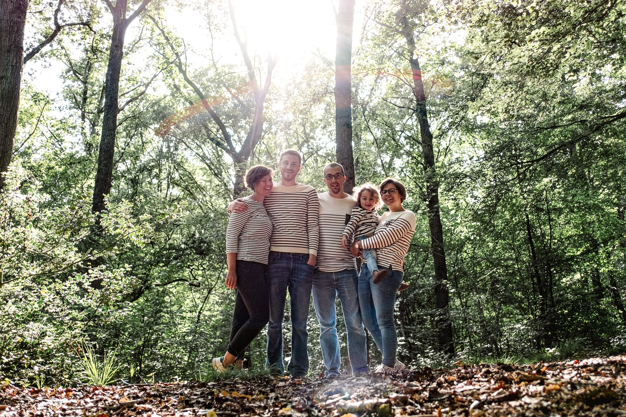 Cinq membres d'une famille réunis dans une forêt sous une lumière en contre-jour.