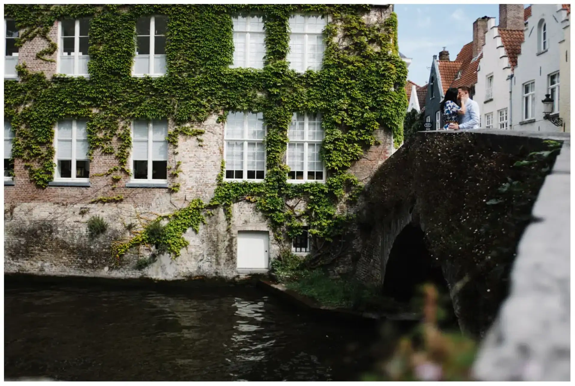 Manon et Jimmy réunis sur un pont au-dessus d'un canal bordé d'une façade couverte de lierre.