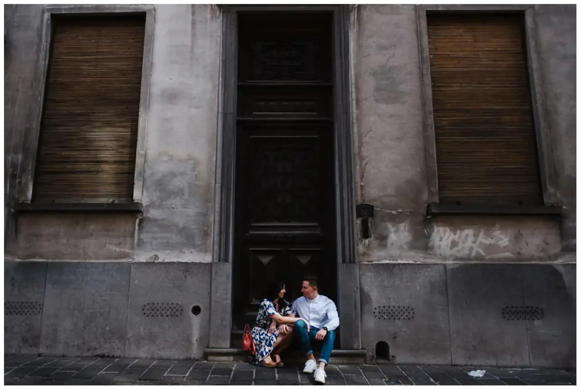 Manon et Jimmy assis sur les marches d'une grande porte sombre dans une rue pavée.