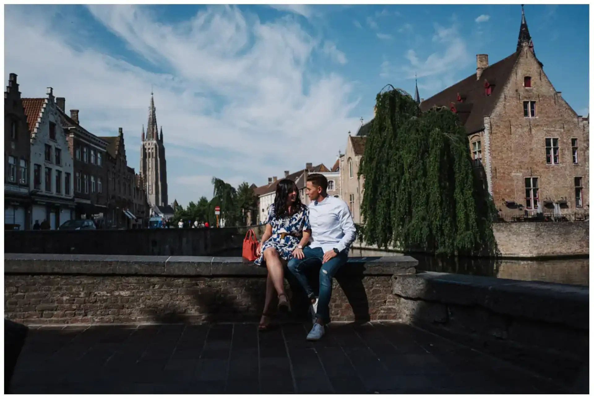 Manon et Jimmy assis sur un quai avec les canaux et les bâtiments anciens de Bruges derrière eux.