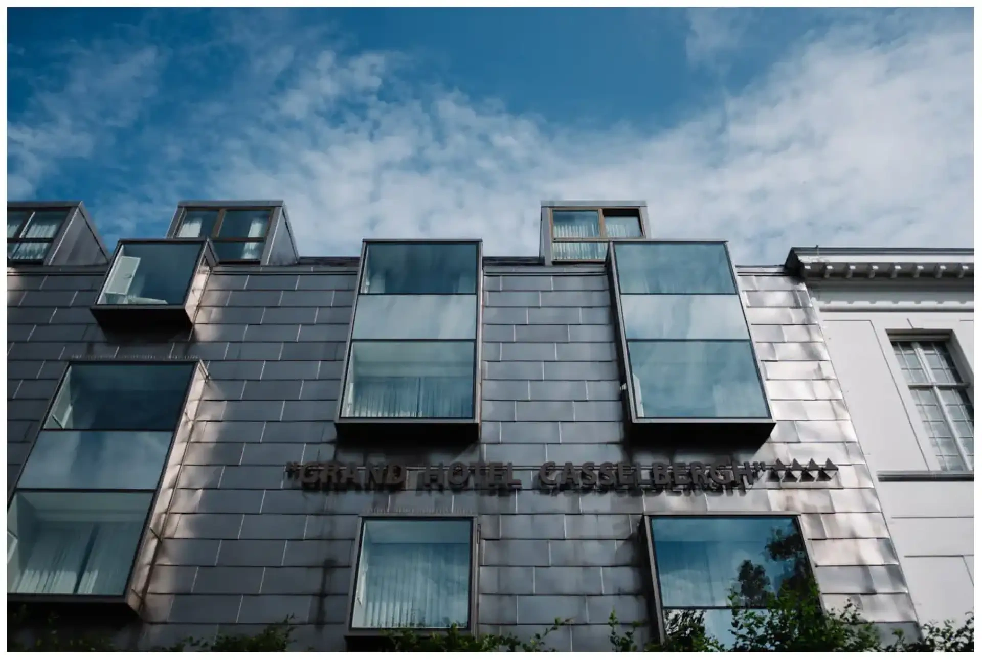 Façade contemporaine vitrée d'un hôtel à Bruges sous un ciel bleu.