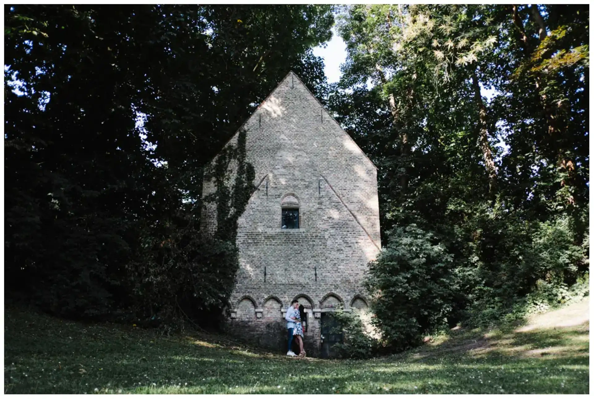 Manon et Jimmy debout au pied d'une haute maison de briques entourée de grands arbres.