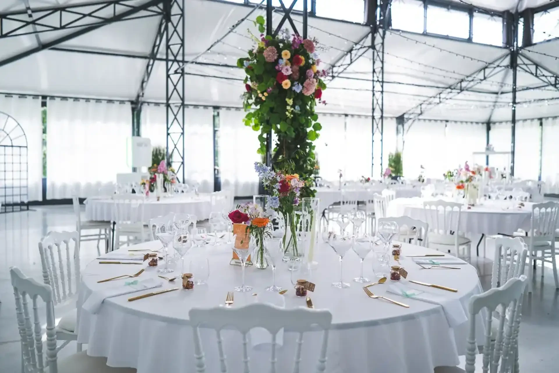 Tables rondes fleuries installées sous la verrière du Clos Barthélemy.