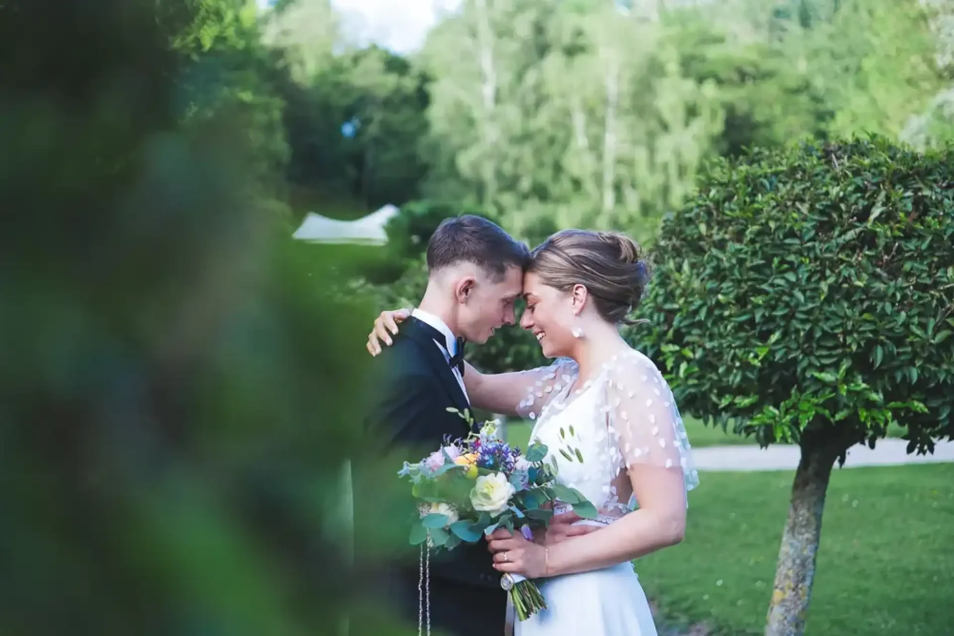 Célia et Louis se regardent dans les jardins avec leurs bouquets au premier plan.