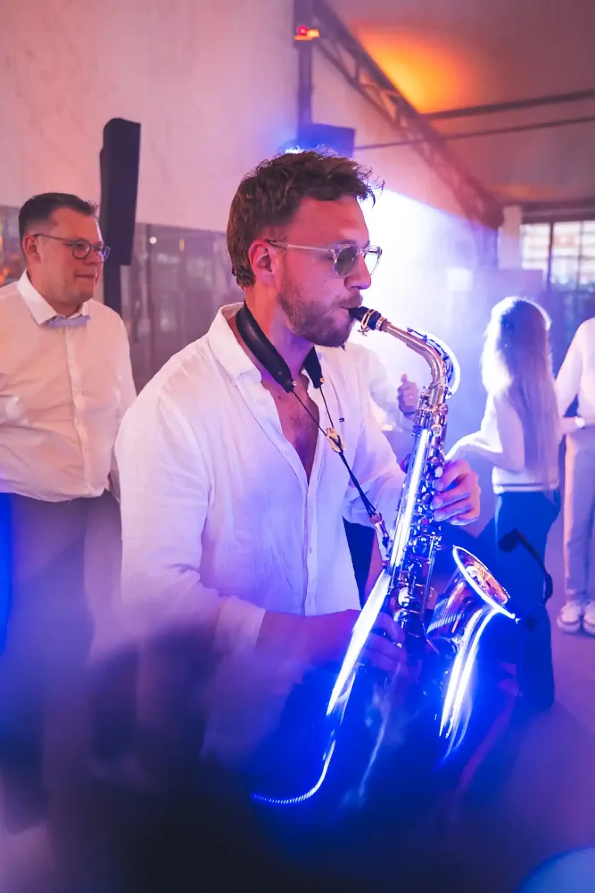 Saxophoniste jouant sous les lumières bleues et violettes de la soirée.