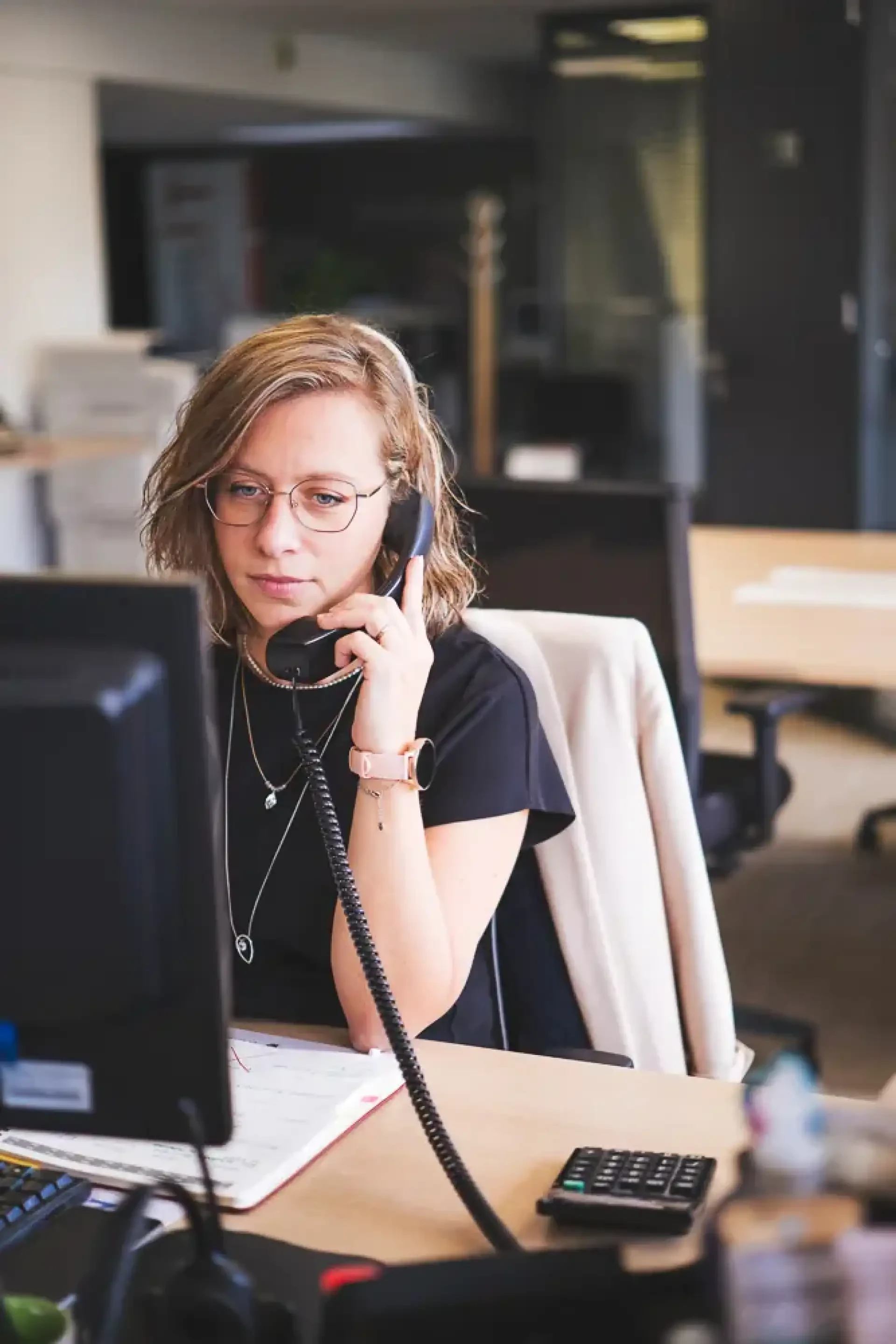 Femme travaillant au téléphone devant son écran dans un bureau.