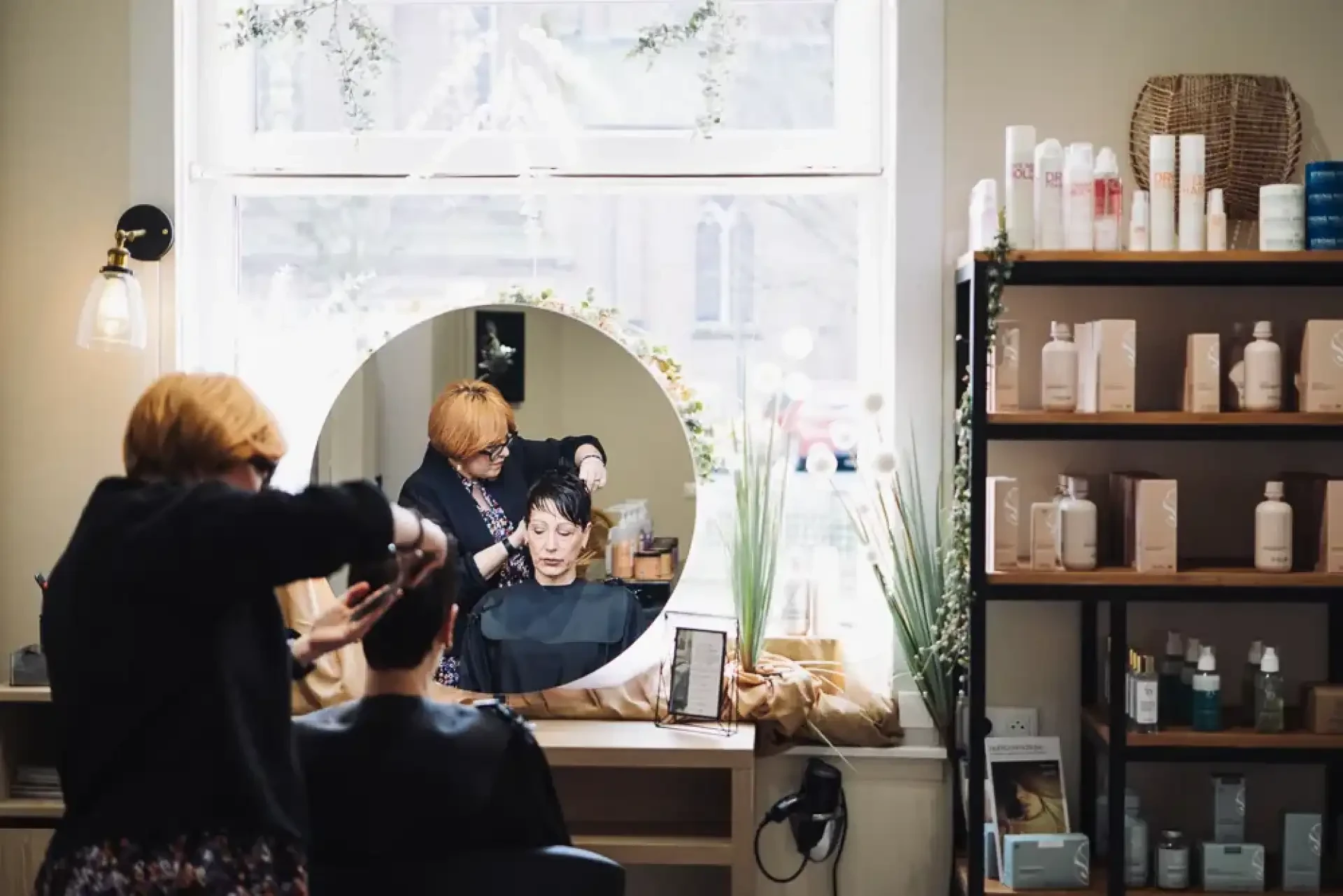Coiffeuse coupant les cheveux d'une cliente face à un miroir.