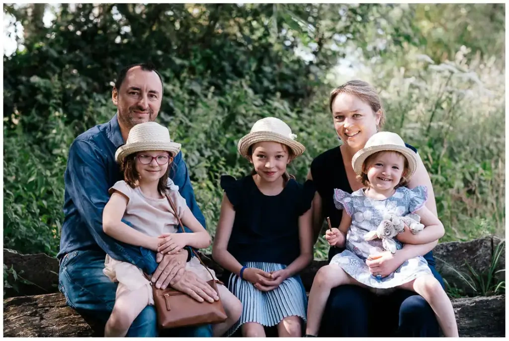 Deux parents et leurs trois filles portant des chapeaux de paille, assis dans un espace boisé.