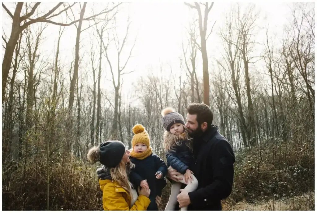 Deux parents et leurs deux jeunes enfants chaudement habillés dans une forêt ensoleillée.