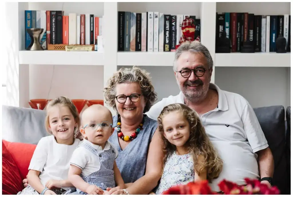 Deux adultes souriants entourés de trois jeunes enfants dans un salon lumineux.