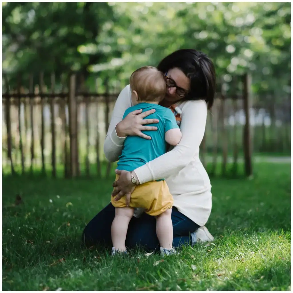 Une femme agenouillée dans l’herbe serre un jeune enfant contre elle.