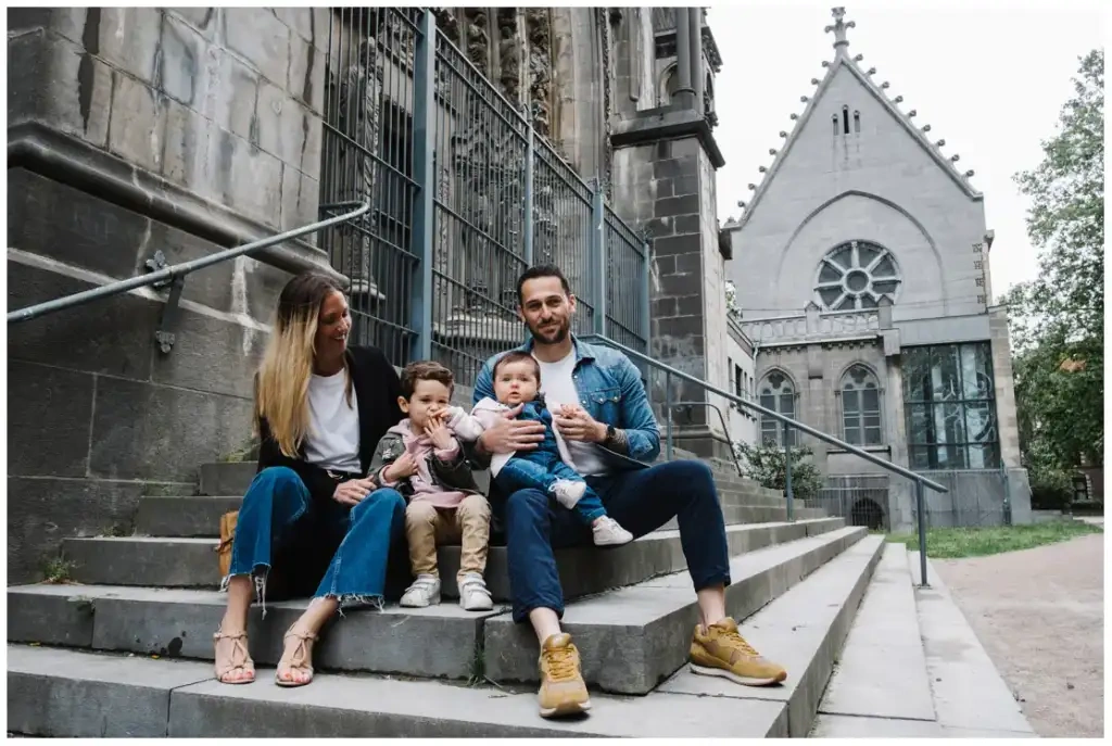 Deux parents et leurs deux jeunes enfants assis sur les marches d’un bâtiment ancien.