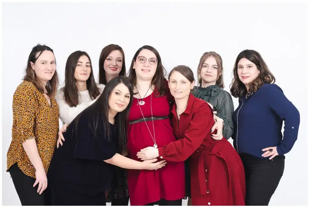 Une future mère en rouge entourée de sept amies lors d'un portrait de groupe.