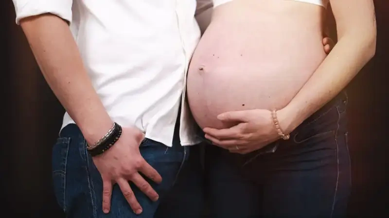 Gros plan sur le ventre d'une femme enceinte et les mains du couple qui l'entourent.