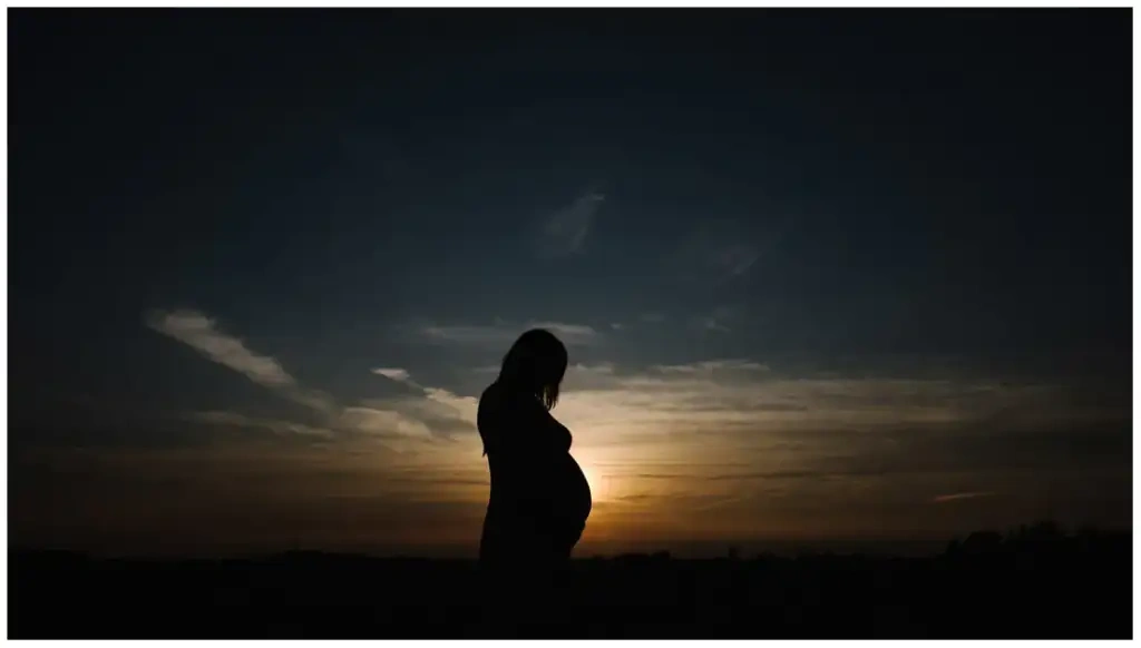 Silhouette d'une femme enceinte de profil devant un coucher de soleil.