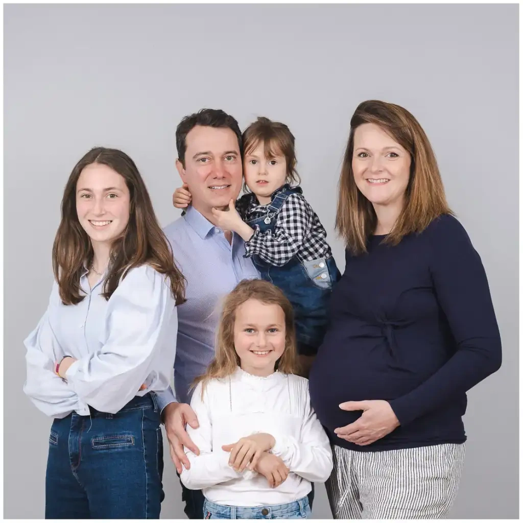 Deux parents et leurs trois filles posent ensemble devant un fond gris.