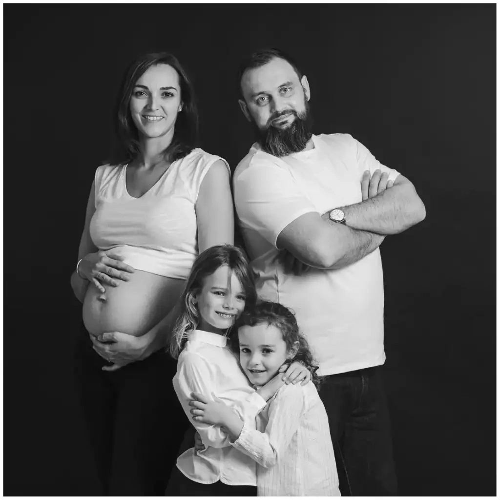 Portrait en noir et blanc de deux parents et de leurs deux filles devant un fond sombre.