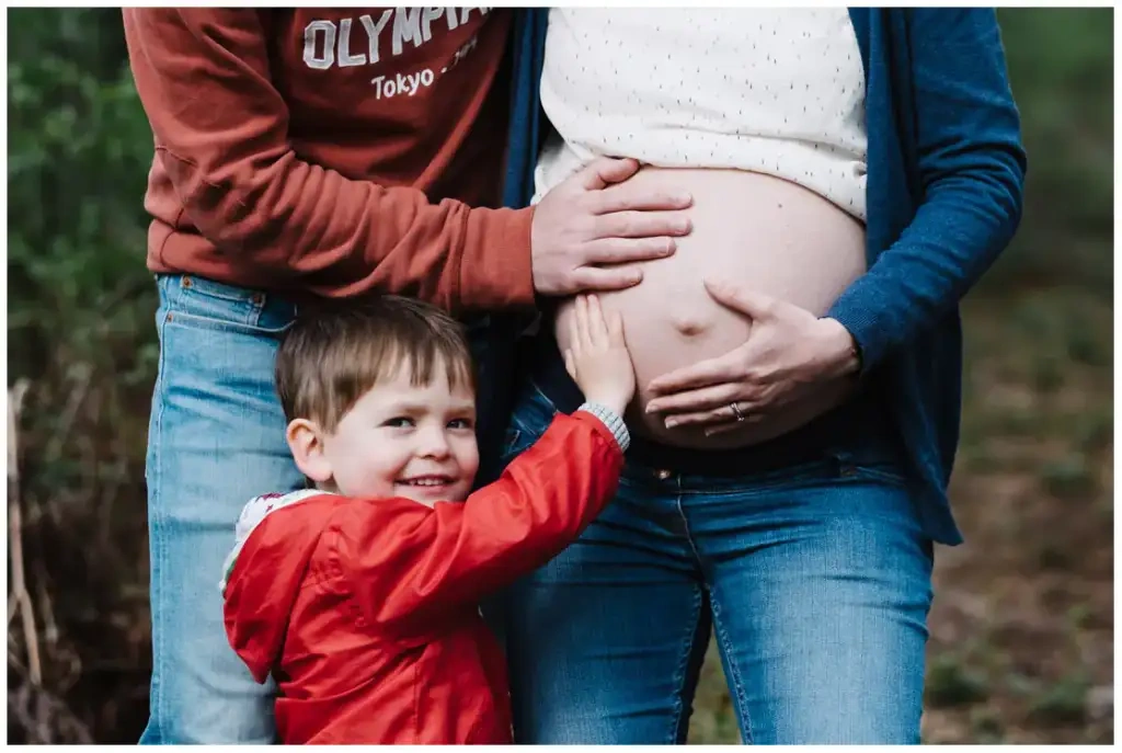 Un jeune garçon en rouge pose sa main sur le ventre de sa mère dans une forêt.