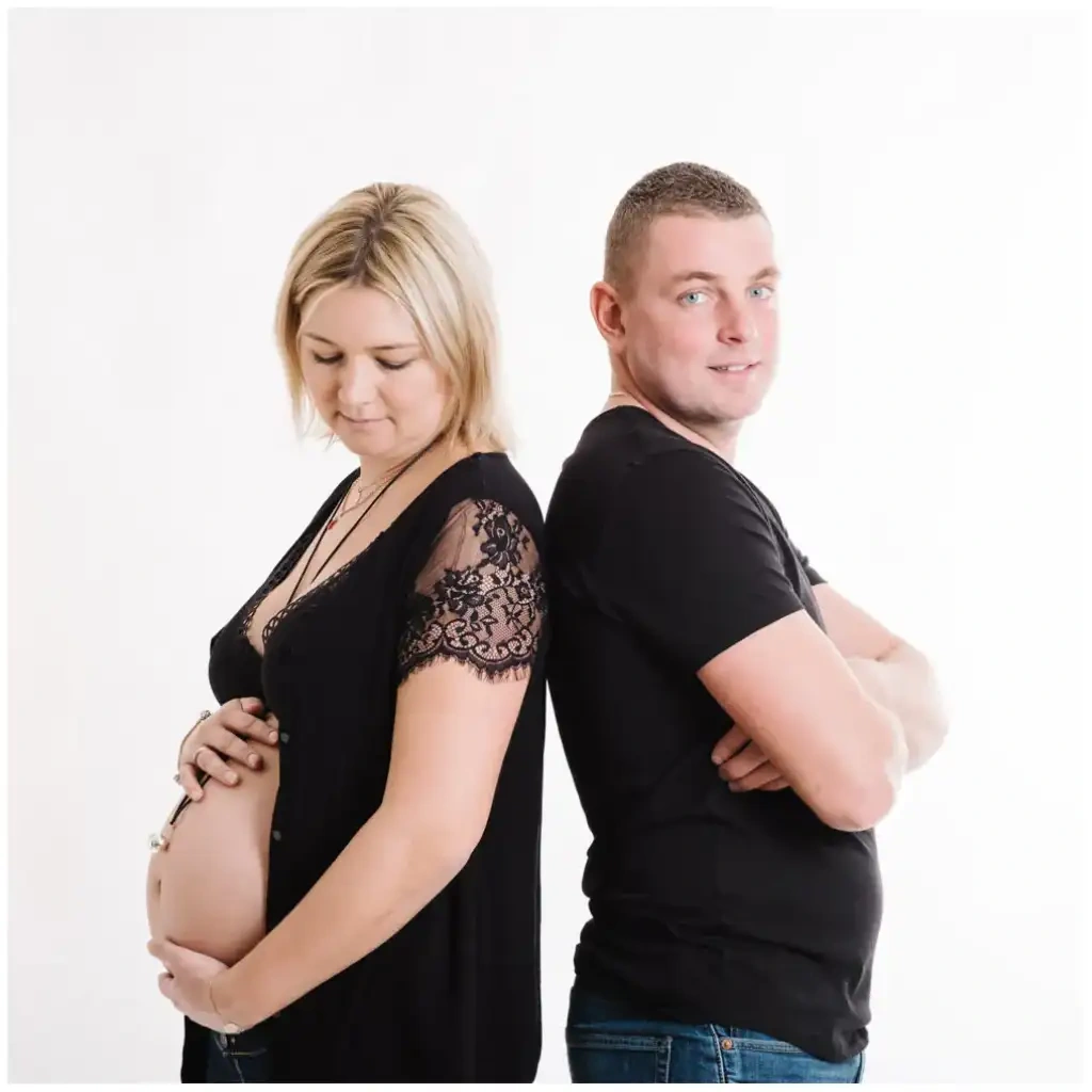 Une femme enceinte et son compagnon posent dos à dos devant un fond blanc.